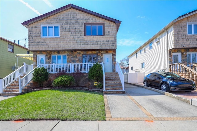 townhome / multi-family property with stairway, stone siding, covered porch, a front lawn, and driveway
