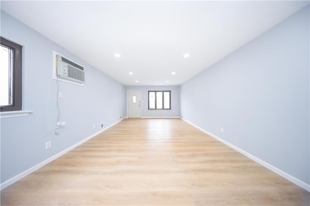 unfurnished living room featuring a wall unit AC, light wood-style flooring, baseboards, and recessed lighting