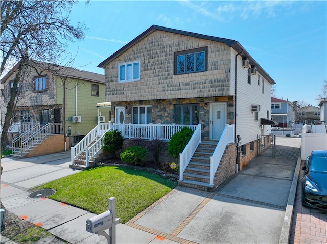 view of front facade with covered porch, stone siding, a front yard, driveway, and stairs