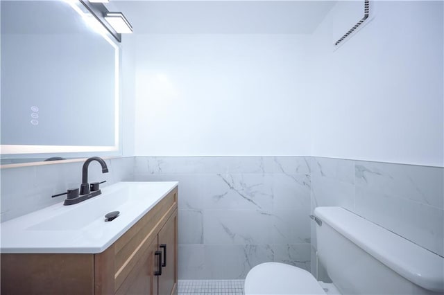 half bath featuring toilet, vanity, tile walls, and a wainscoted wall