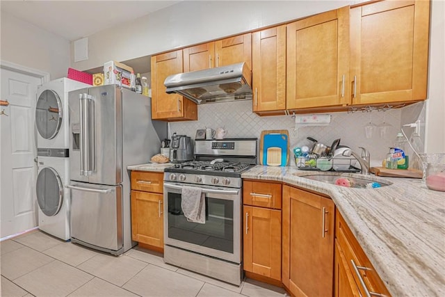 kitchen with backsplash, under cabinet range hood, a sink, appliances with stainless steel finishes, and stacked washer / drying machine