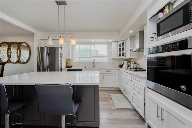 kitchen featuring wall chimney range hood, stainless steel appliances, a sink, and a breakfast bar area