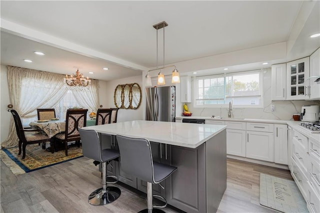kitchen with freestanding refrigerator, a breakfast bar, light wood-type flooring, white cabinets, and a sink