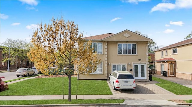 view of front facade with french doors, stucco siding, driveway, and a front yard