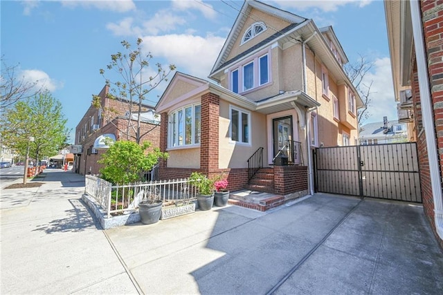 view of front of house featuring brick siding, a gate, stucco siding, and fence