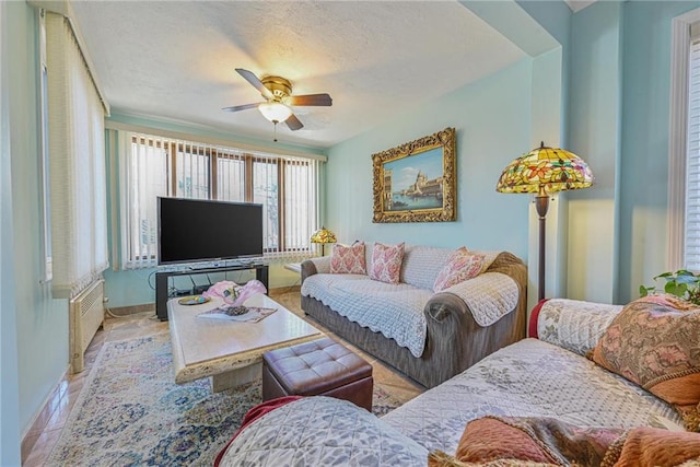 living area featuring radiator heating unit, baseboards, a ceiling fan, and a textured ceiling
