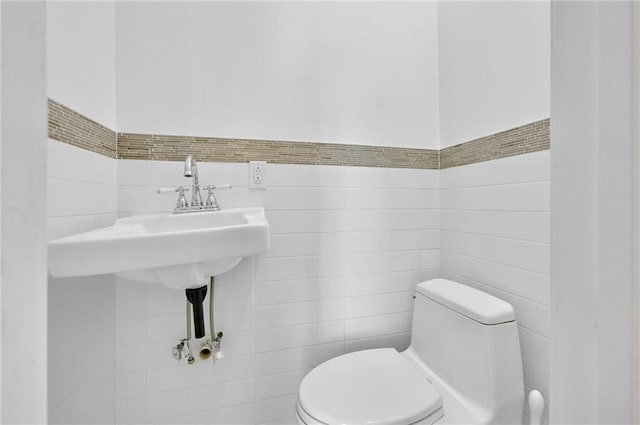 half bath with tile walls, wainscoting, and toilet