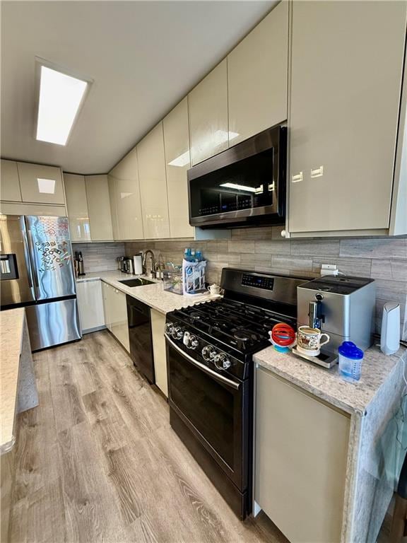 kitchen featuring light wood-style floors, modern cabinets, a sink, backsplash, and black appliances
