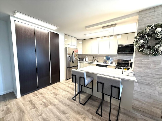 kitchen with a breakfast bar, a sink, light countertops, stainless steel appliances, and backsplash