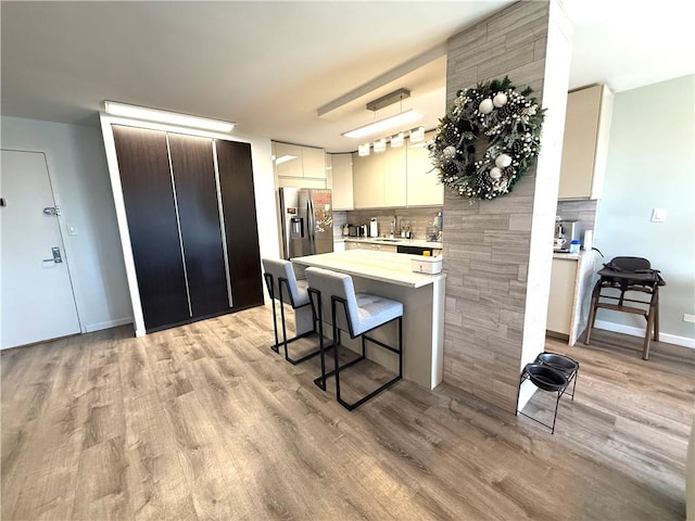 kitchen featuring a breakfast bar area, stainless steel refrigerator with ice dispenser, light countertops, tasteful backsplash, and a sink