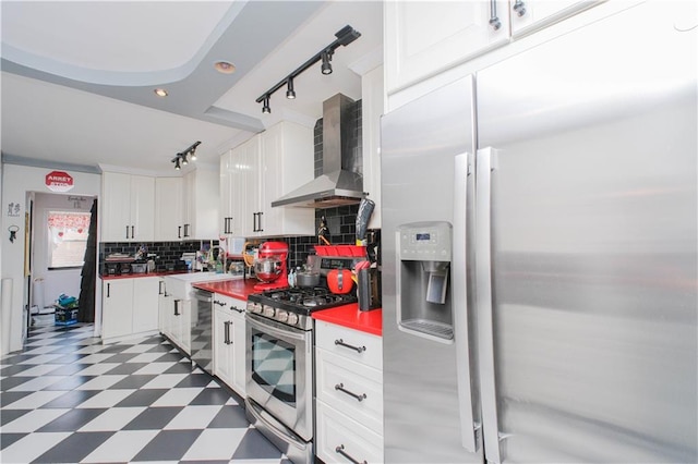 kitchen with stainless steel appliances, wall chimney range hood, track lighting, tile patterned floors, and backsplash