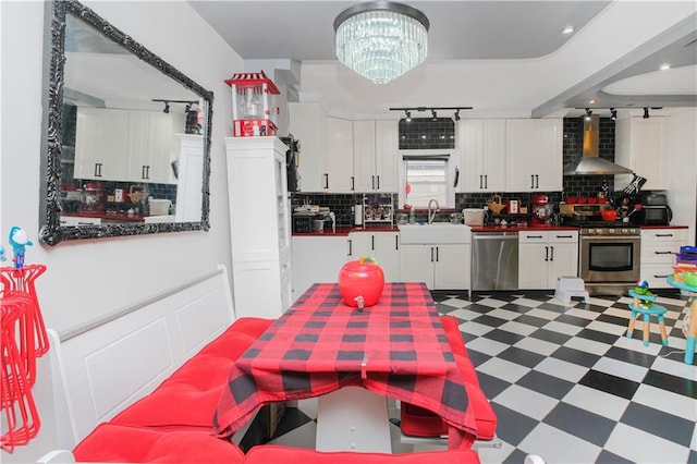 kitchen with light floors, track lighting, wall chimney exhaust hood, white cabinetry, and appliances with stainless steel finishes