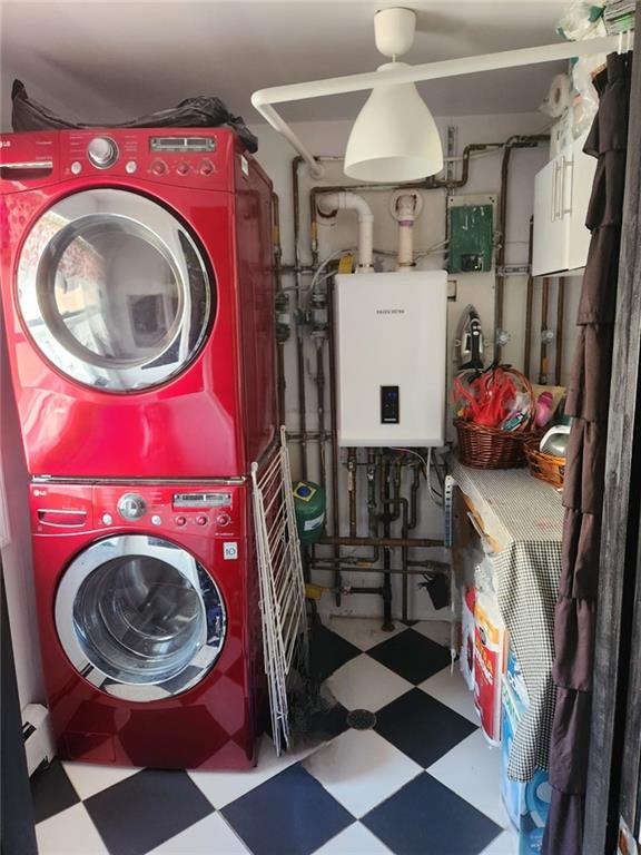 clothes washing area featuring laundry area, stacked washer and clothes dryer, tankless water heater, and tile patterned floors