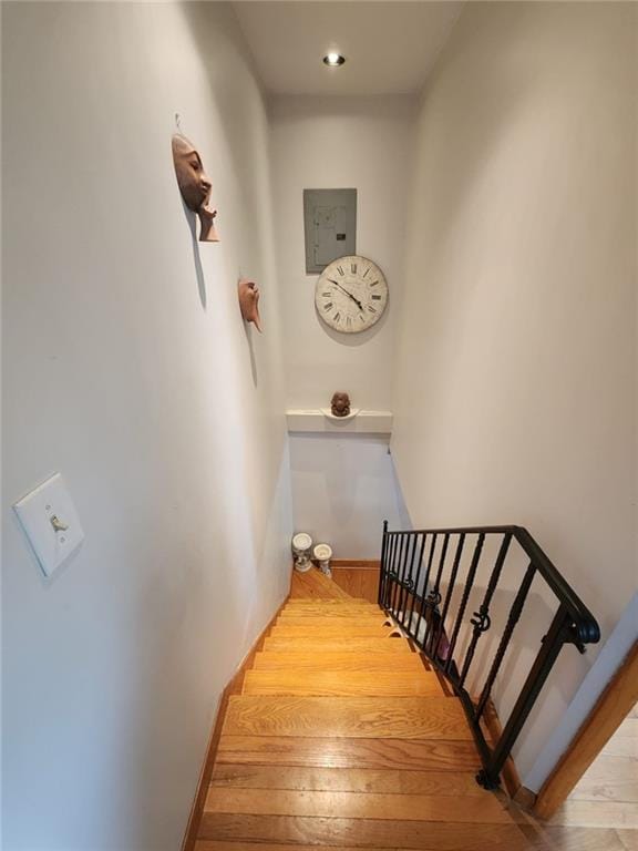 stairway with baseboards, electric panel, and wood finished floors