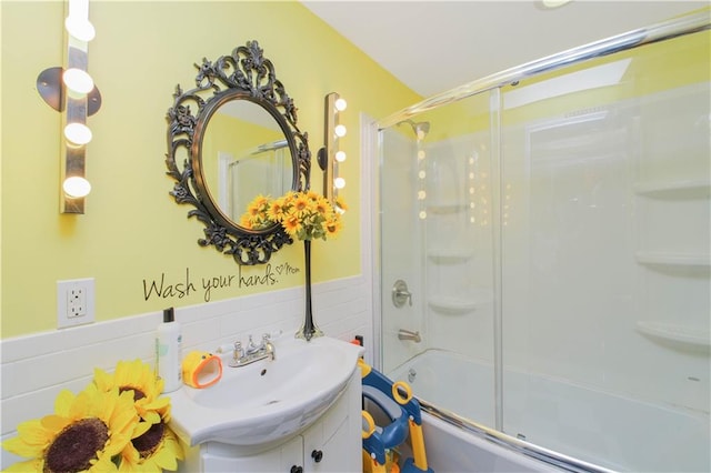 full bath featuring vanity, tile walls, wainscoting, and shower / bath combination with glass door