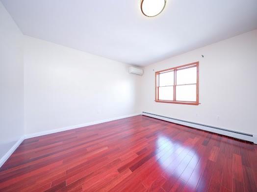 299 Bay 13th St, Brooklyn, NY 11214 - empty room with a baseboard radiator, a wall mounted air conditioner, wood finished floors, and baseboards