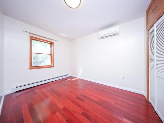 299 Bay 13th St, Brooklyn, NY 11214 - unfurnished bedroom featuring baseboard heating, an AC wall unit, wood finished floors, a closet, and lofted ceiling