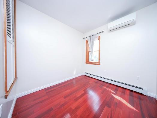 299 Bay 13th St, Brooklyn, NY 11214 - spare room with a wall mounted AC, a baseboard radiator, wood finished floors, and baseboards