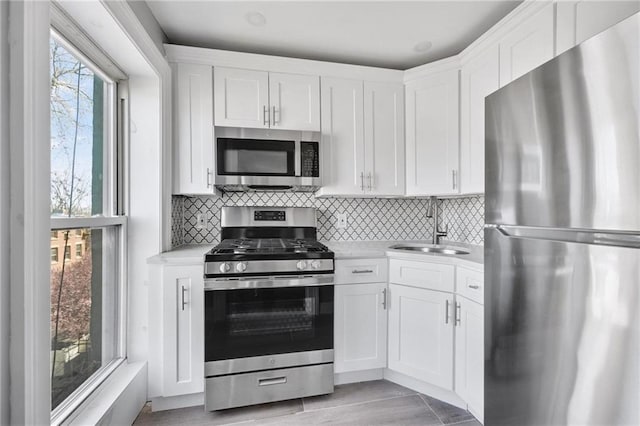 kitchen featuring decorative backsplash, appliances with stainless steel finishes, a sink, light countertops, and white cabinetry