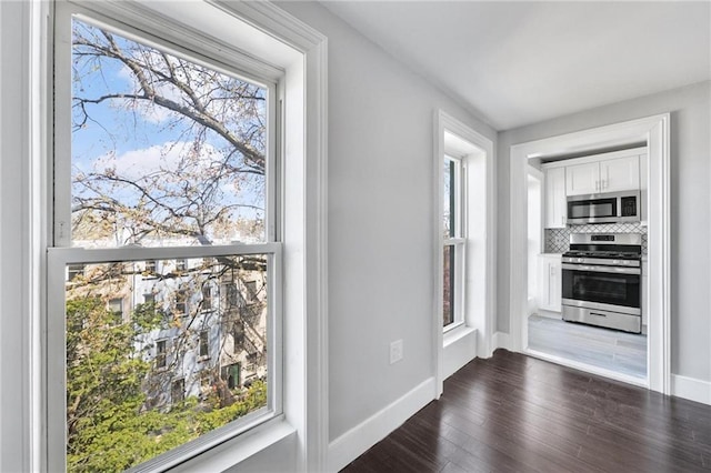 kitchen with a healthy amount of sunlight, appliances with stainless steel finishes, white cabinets, and dark wood-style flooring