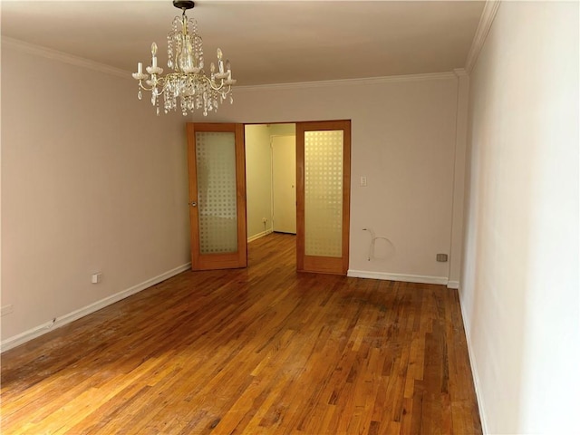 unfurnished room featuring a chandelier, wood finished floors, ornamental molding, and baseboards