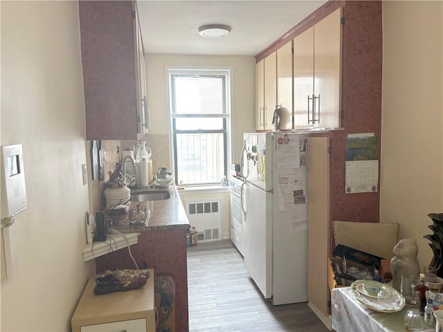 kitchen featuring a sink, radiator heating unit, light wood finished floors, and freestanding refrigerator