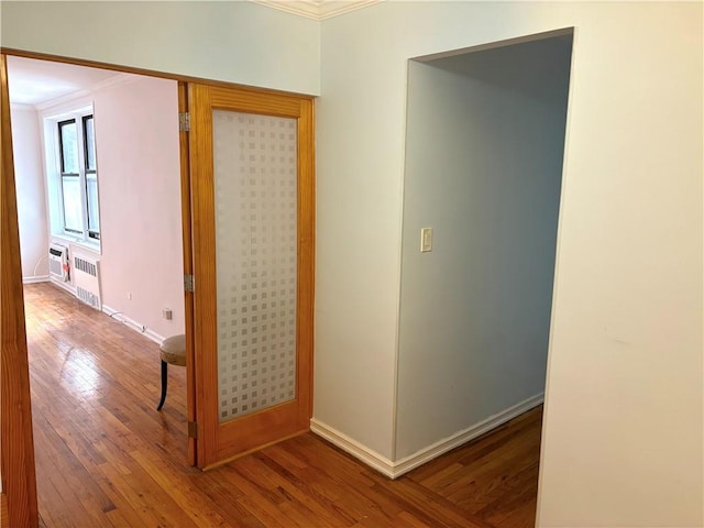 hallway featuring crown molding, hardwood / wood-style floors, baseboards, and radiator heating unit