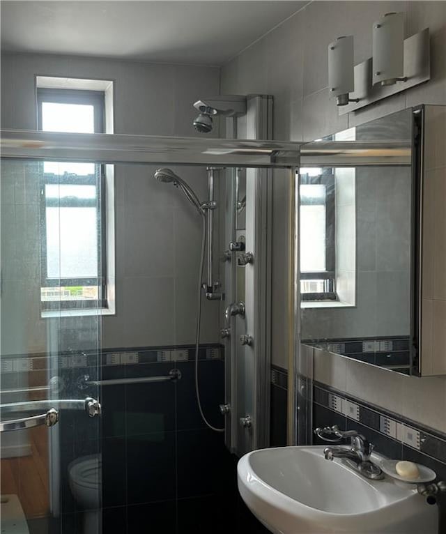 full bath featuring a sink, a shower stall, tile walls, and toilet