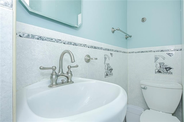 bathroom featuring toilet, tile walls, and a sink