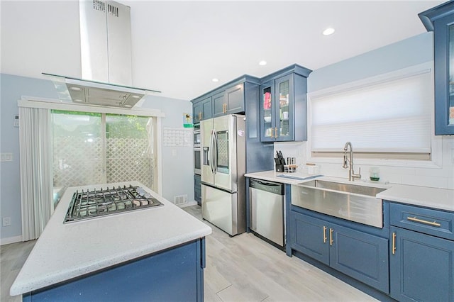 kitchen featuring appliances with stainless steel finishes, a sink, blue cabinetry, light wood-style flooring, and island exhaust hood