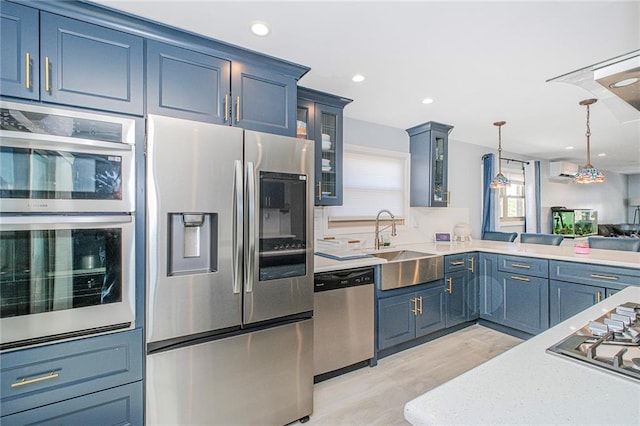 kitchen featuring pendant lighting, appliances with stainless steel finishes, light wood-type flooring, a sink, and glass insert cabinets