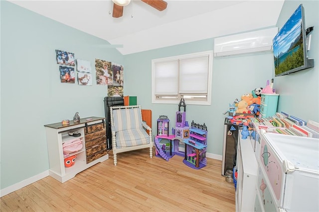 playroom featuring baseboards, light wood finished floors, ceiling fan, and a wall unit AC