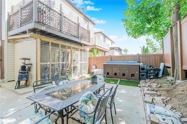 view of patio with a fenced backyard, outdoor dining space, a hot tub, and a balcony