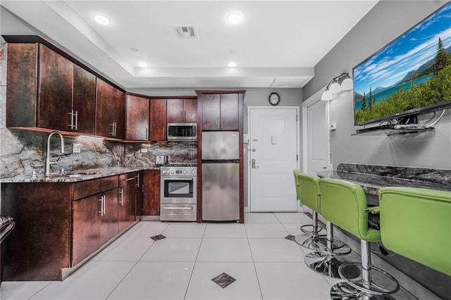 kitchen with appliances with stainless steel finishes, a sink, dark stone counters, decorative backsplash, and visible vents