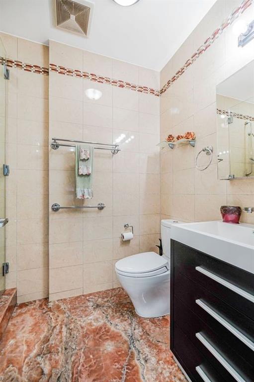 bathroom featuring vanity, toilet, tile walls, visible vents, and a stall shower