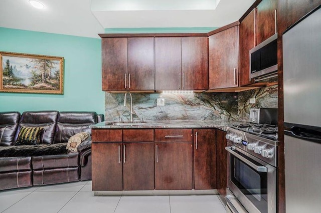 kitchen with a sink, stainless steel appliances, stone counters, light tile patterned floors, and backsplash
