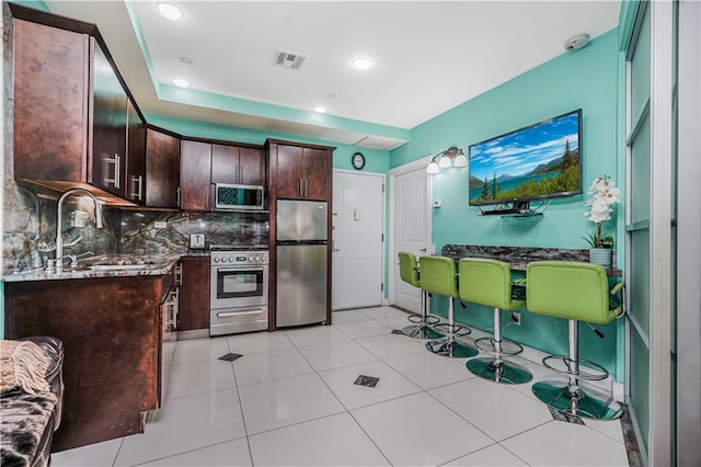 kitchen with dark brown cabinetry, a sink, stainless steel appliances, backsplash, and visible vents