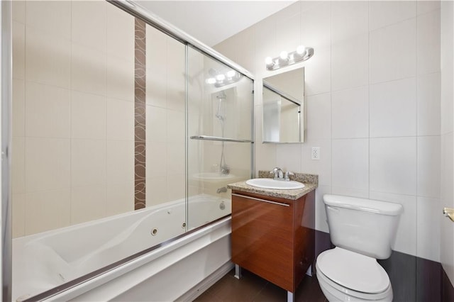 bathroom featuring vanity, enclosed tub / shower combo, toilet, and tile walls