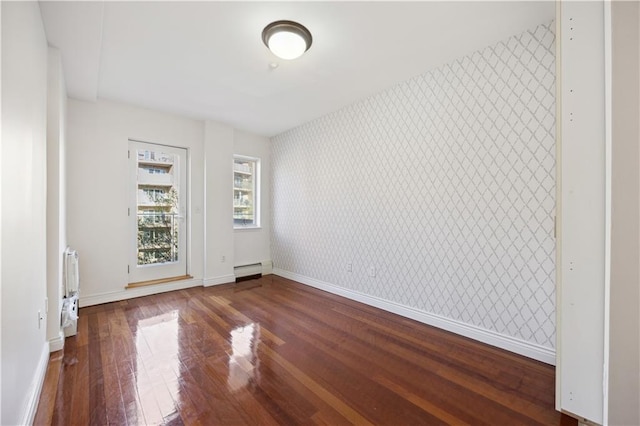 empty room featuring baseboards, a baseboard radiator, wallpapered walls, and hardwood / wood-style floors