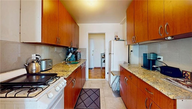kitchen with brown cabinets, light stone countertops, white gas range oven, light tile patterned floors, and tasteful backsplash