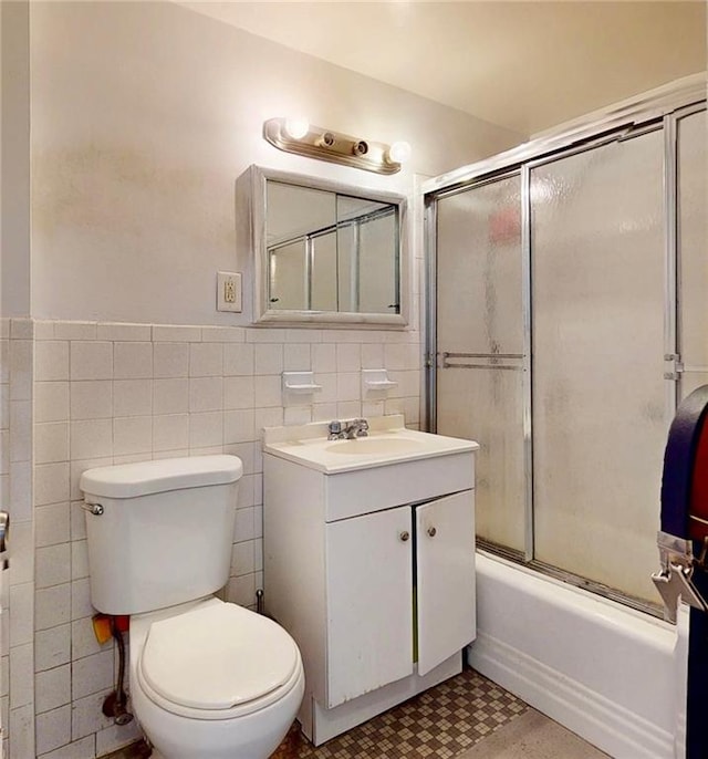 bathroom with vanity, wainscoting, toilet, tile walls, and enclosed tub / shower combo