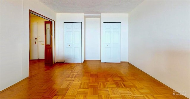 unfurnished bedroom with a textured ceiling and multiple closets