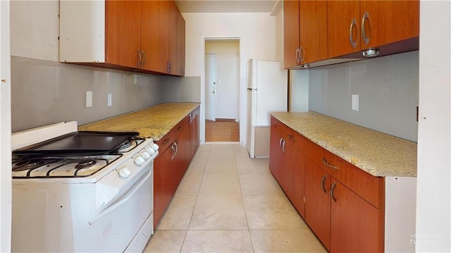 kitchen with brown cabinetry, white appliances, and light tile patterned flooring