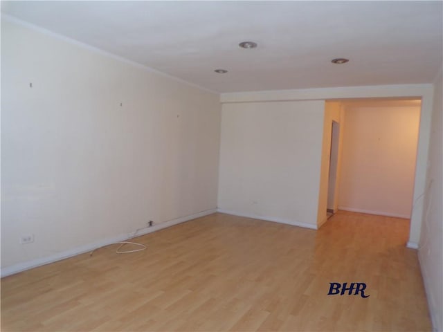 empty room featuring crown molding, baseboards, and light wood-type flooring