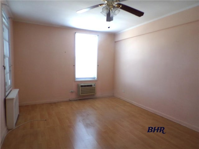 empty room featuring a ceiling fan, a wall mounted AC, baseboards, light wood finished floors, and radiator