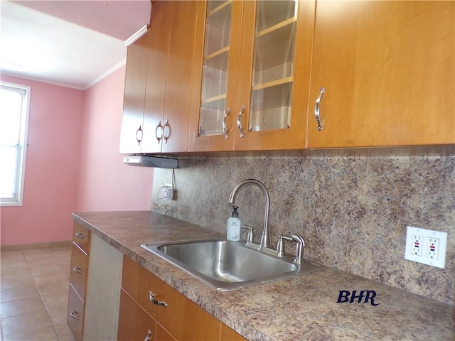 kitchen featuring crown molding, a sink, brown cabinetry, tasteful backsplash, and glass insert cabinets