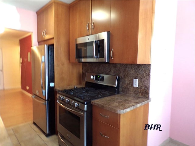 kitchen with decorative backsplash, appliances with stainless steel finishes, brown cabinets, and dark countertops