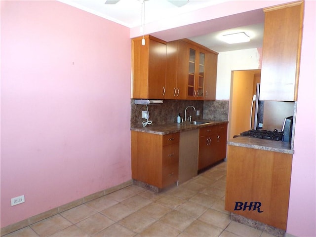 kitchen with a ceiling fan, baseboards, brown cabinets, a sink, and backsplash