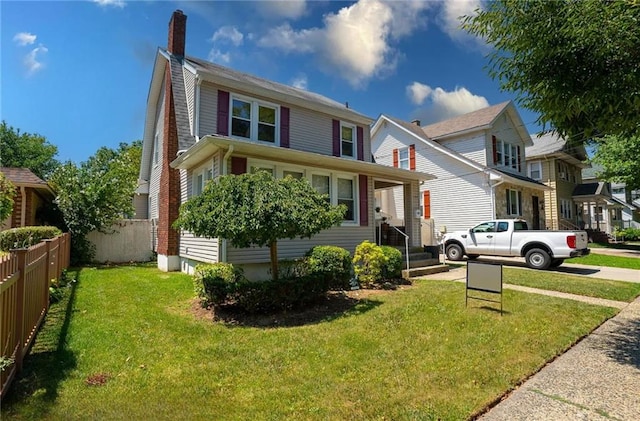 american foursquare style home featuring fence, a chimney, and a front yard
