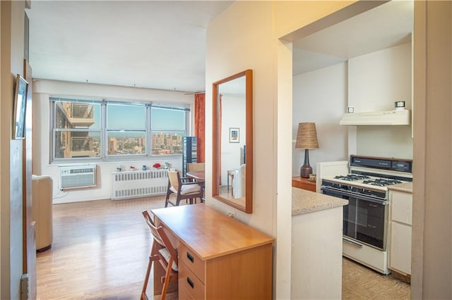 448 Neptune Ave Unit 19A, Brooklyn, NY 11224 - kitchen with radiator, white gas range, light countertops, a wall mounted AC, and under cabinet range hood